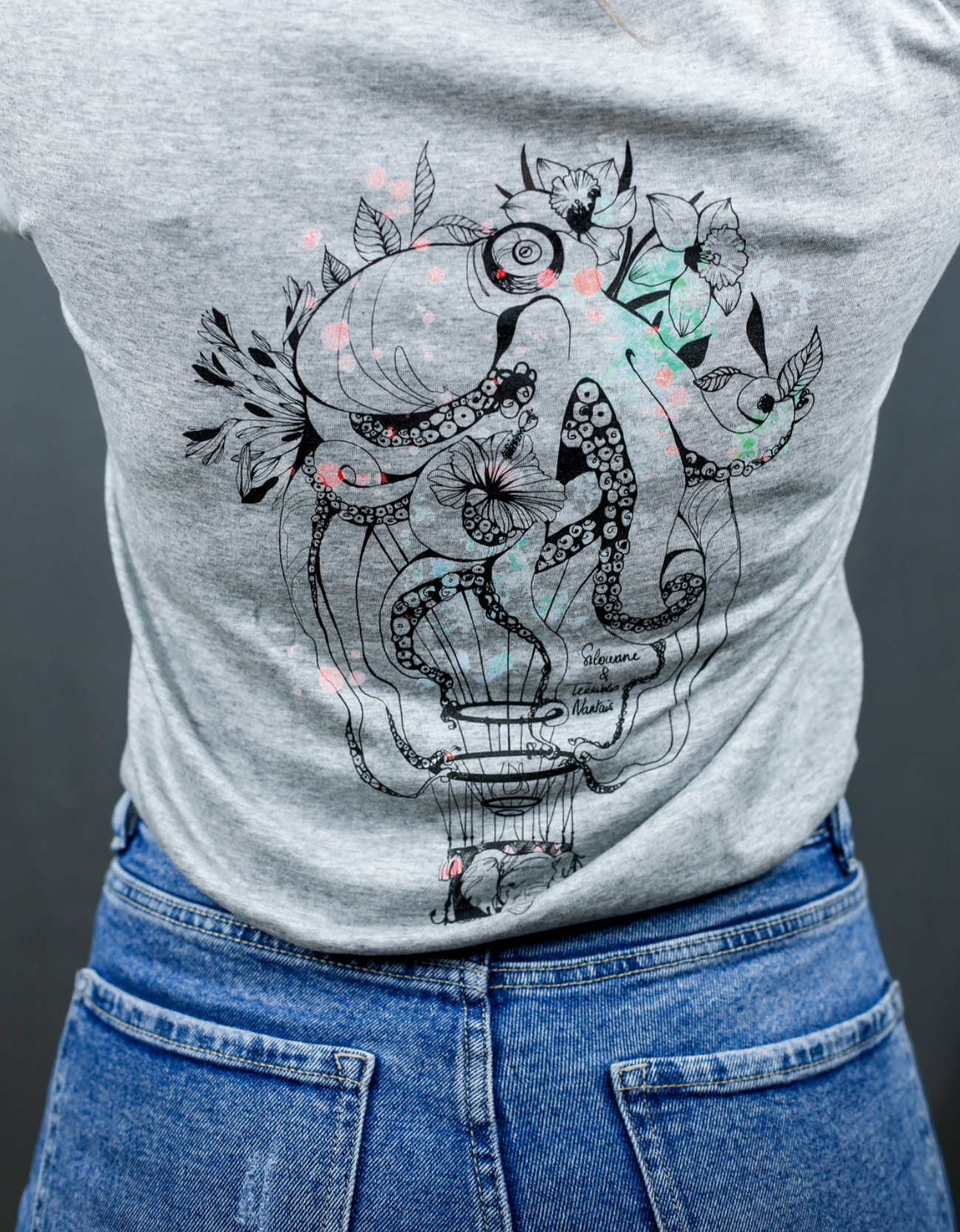 Femme avec T-Shirt gris à col V et visuel noir, vert et rouge de la marque Terribles Nantais