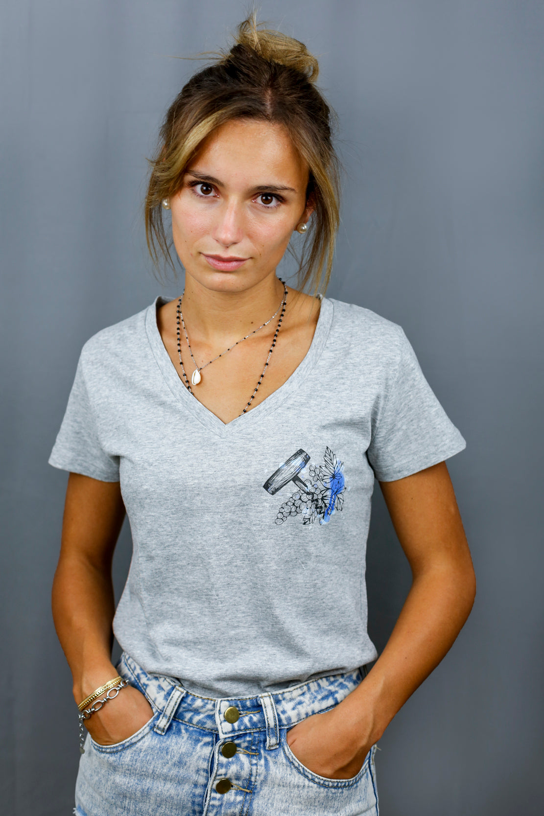 Femme avec T-Shirt gris à col V et visuel noir, bleu et bleu clair de la marque Terribles Nantais