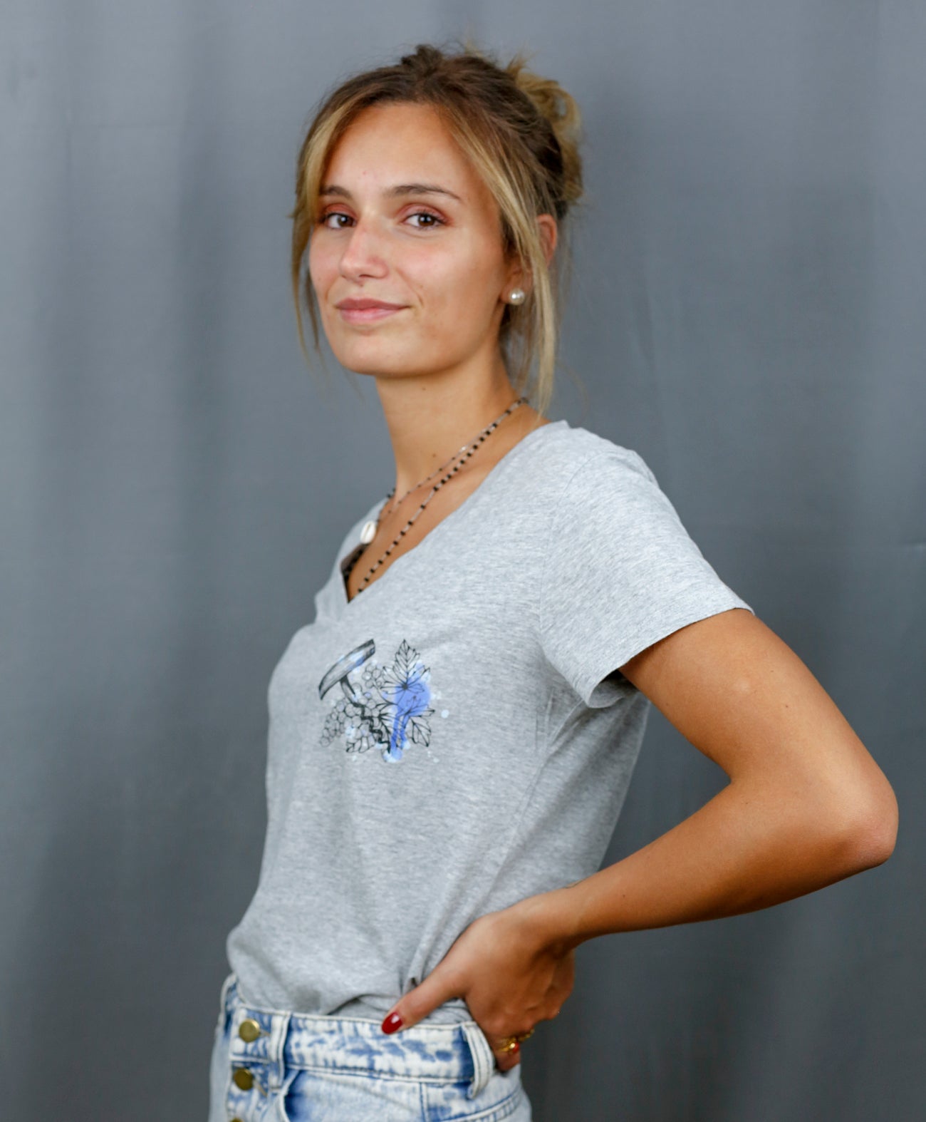 Femme avec T-Shirt gris à col V et visuel noir, bleu et bleu clair de la marque Terribles Nantais