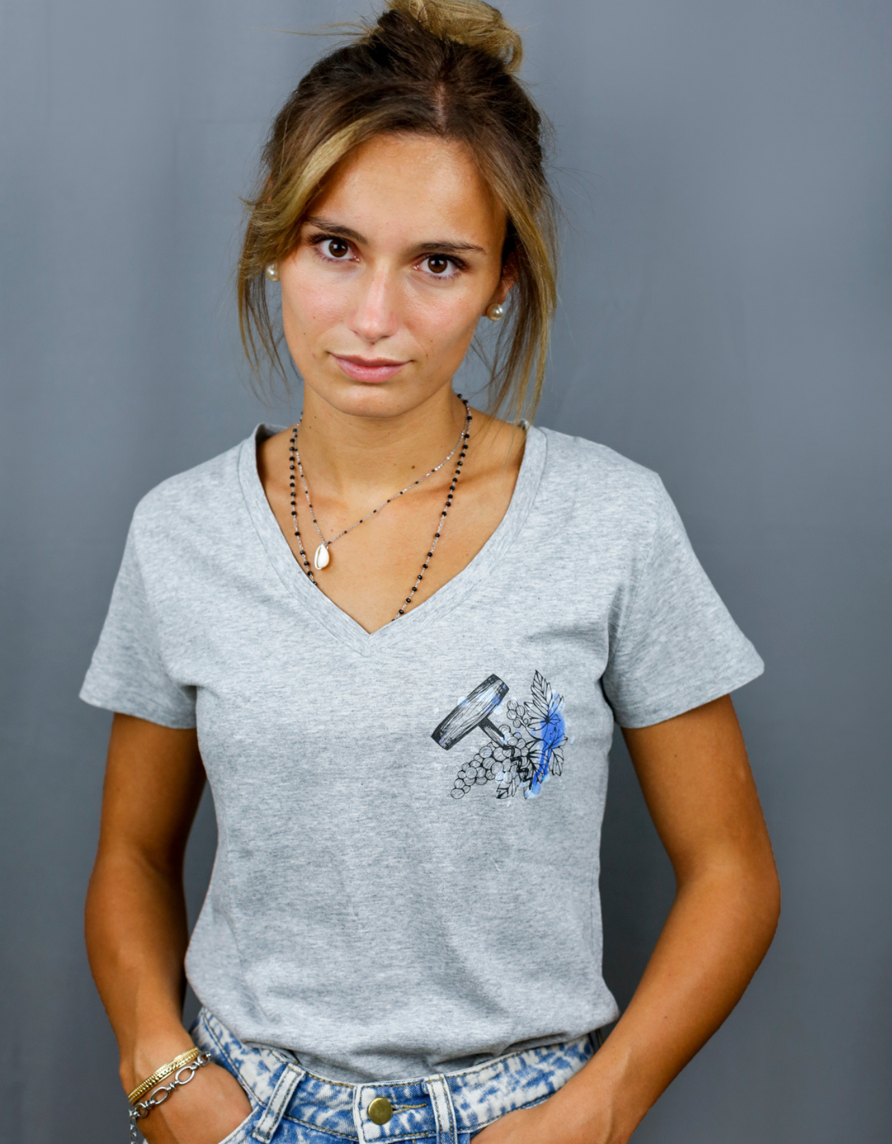Femme avec T-Shirt gris à col V et visuel noir, bleu et bleu clair de la marque Terribles Nantais