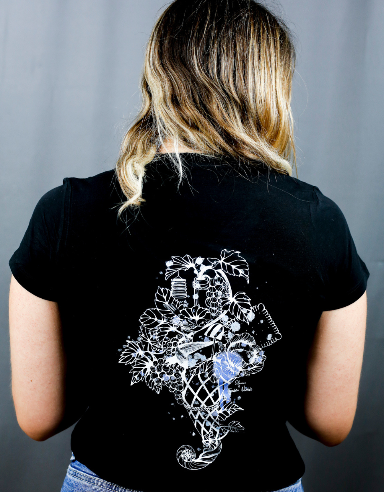 Femme avec T-Shirt noir à col V et visuel blanc, bleu et bleu clair de la marque Terribles Nantais